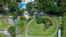 Aerial perspective featuring an expansive lot with mature trees, a swimming pool, a pond, and paved pathways
