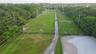 Expansive grounds featuring a central paved driveway, perimeter post-and-rail fencing, a dedicated sand ring, and mature tree buffers