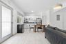 Open living and dining area with a wood dining table, black chairs, white kitchenette cabinetry, a stainless steel refrigerator and a louvered closet 