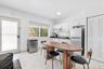 Kitchenette featuring white cabinetry, contrasting dark countertops, a stainless steel refrigerator, white tile flooring and a closet with louvered do