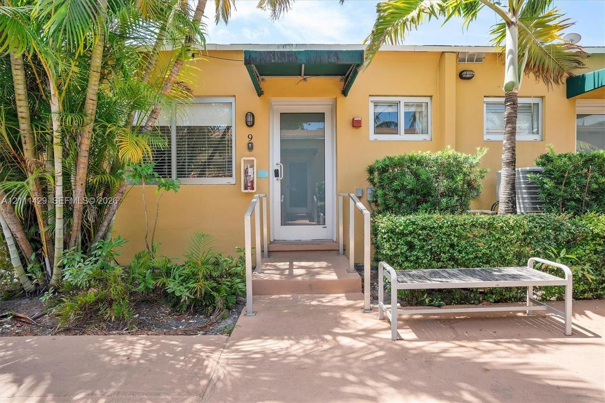 Stucco exterior featuring a glass-panel entry door, metal handrails, fixed green awnings, and low-maintenance landscaping