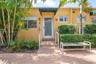 Stucco exterior featuring a glass-panel entry door, metal handrails, fixed green awnings, and low-maintenance landscaping