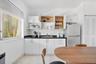 Kitchen featuring white shaker-style cabinetry, dark solid-surface countertops, stainless steel refrigerator, white tile flooring, and horizontal wind