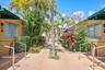 Courtyard featuring paved walkways, mature palm trees, tiered shrubbery, and dark green fabric awnings