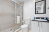 Bathroom featuring a walk-in shower with glass enclosure and large-format tile surround, vanity with dark countertop, integrated sink, and wall-mounte