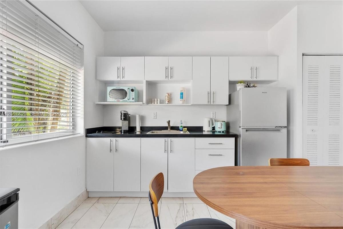 Kitchen featuring white cabinetry, dark countertops, tile flooring, stainless steel refrigerator, and horizontal window blinds