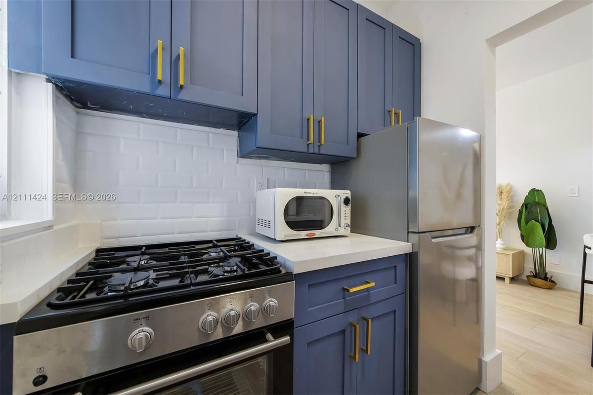 Kitchen featuring blue cabinetry with metallic hardware, light-toned countertop, white subway tile backsplash, and stainless steel gas range