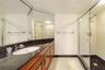 Vanity with dark countertop and white oval under-mount sink, wood-finish cabinetry, floor-to-ceiling mirror, and glass-enclosed shower with tiled floo