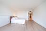 Expansive room featuring light-toned wood-finish flooring, smooth white walls, and high ceilings