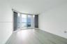 Floor-to-ceiling windows, sliding glass door, wood-finish flooring, and balcony access with water backdrop