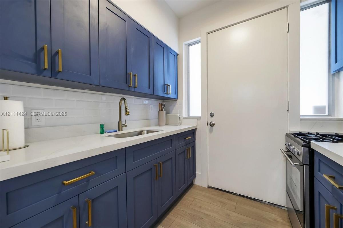 Kitchen featuring navy blue Shaker-style cabinetry, matte gold hardware, white subway tile backsplash, solid-surface countertops, and wood-finish floo