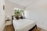 Neutral-toned interior featuring wood-finish flooring, a wall-mounted floating shelf, and a sliding window with outdoor greenery