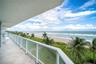 Covered balcony featuring tile flooring and a glass-paneled railing overlooking the ocean, sandy beach, and palm trees