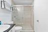Walk-in shower featuring sliding glass doors, neutral tile surround, black countertop vanity, integrated shelving, and polished hardware