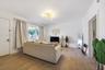 Living area featuring light-tone wood-finish flooring, recessed multi-arm ceiling light fixture, large window with neutral drapery, and crisp white wa