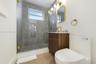 Walk-in shower with floor-to-ceiling stone-finish tile, glass enclosure, and wood-finish vanity featuring brushed brass fixtures, integrated wall-moun