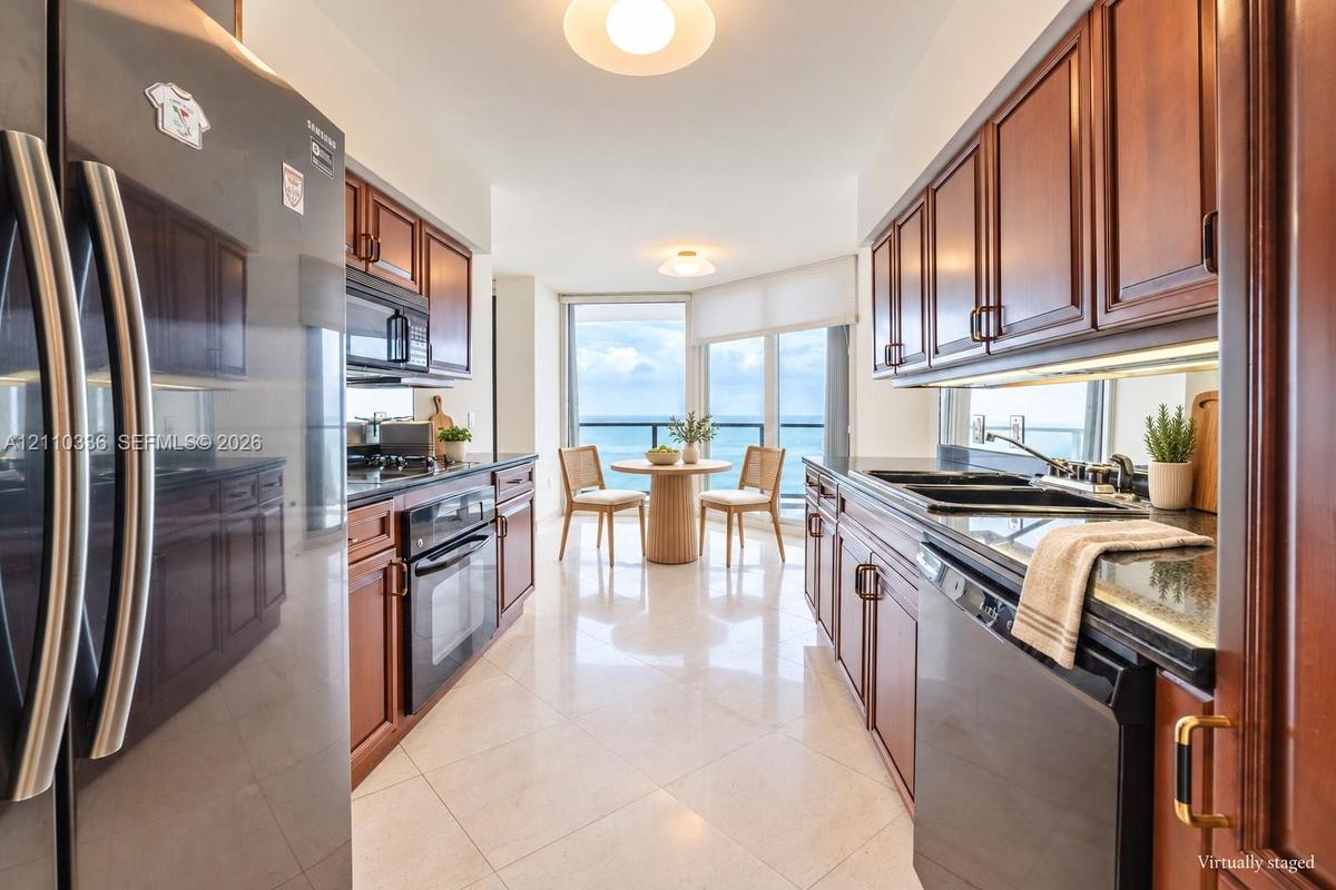 Galley kitchen featuring rich wood cabinetry, stone countertops, stainless steel appliances, and large-format tile flooring, complemented by expansive
