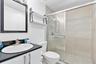 Bathroom featuring a vanity with a dark countertop and integrated sink, a framed mirror, a wall-mounted shelf, and a walk-in shower with a glass door 
