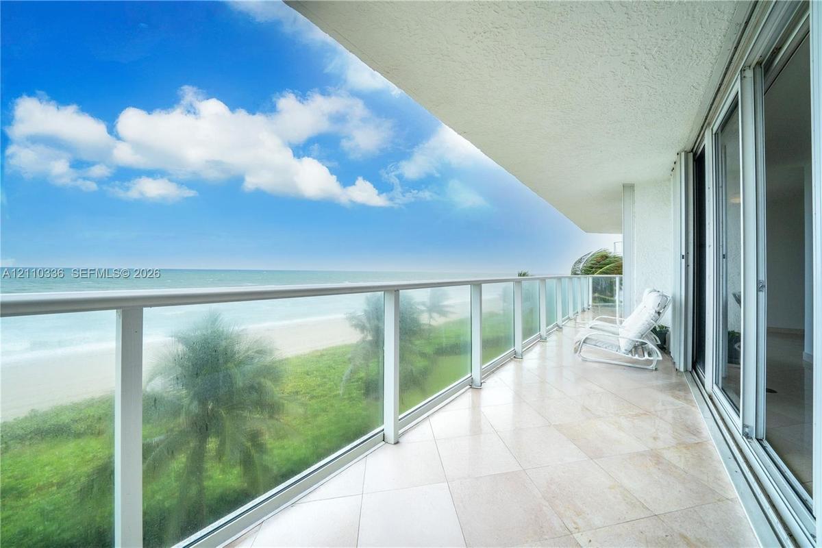 Covered balcony featuring stone tile flooring and a glass railing, encompassing water scenery