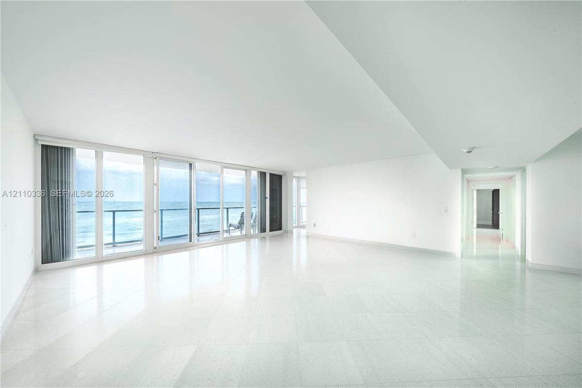 Open-concept interior featuring polished stone flooring, floor-to-ceiling glass sliding doors, and a private balcony with metal railing