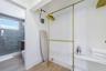 Storage area featuring gold-tone metal garment rods, white shelving, and wood-finish flooring, with a partial look at a bathroom containing large-form