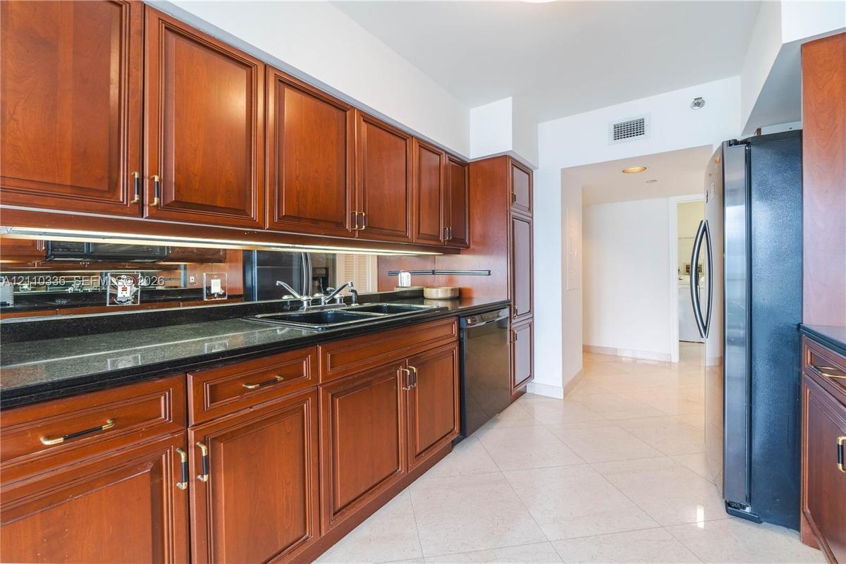 Kitchen featuring raised-panel wood cabinetry, black countertops, mirrored backsplash, under-cabinet lighting, and black appliances