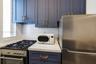 Kitchen featuring blue shaker-style cabinetry with brass-finish hardware, solid-surface countertops, white subway tile backsplash, and stainless steel