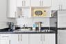 Kitchenette featuring white cabinetry with brushed-metal pulls, solid-surface dark countertops, a stainless steel undermount sink, and an integrated e