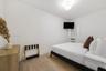 Neutral-toned room featuring wood-finish flooring, a wall-mounted climate control unit, and a flush-mount ceiling light fixture
