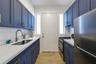 Galley kitchen featuring matte blue shaker-style cabinetry, gold-tone hardware, white subway tile backsplash, solid-surface countertops, and wood-fini