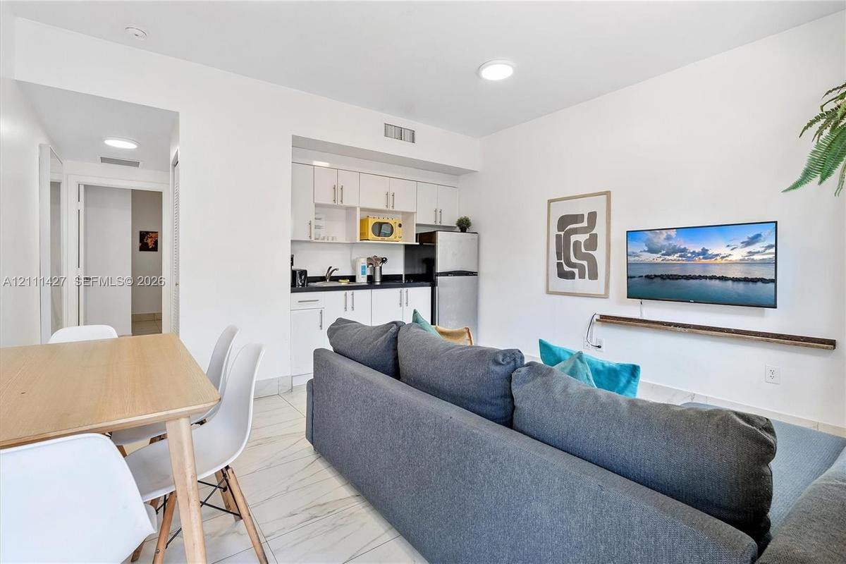 White shaker-style cabinetry, dark stone countertops, tile flooring, and wall-mounted floating shelf