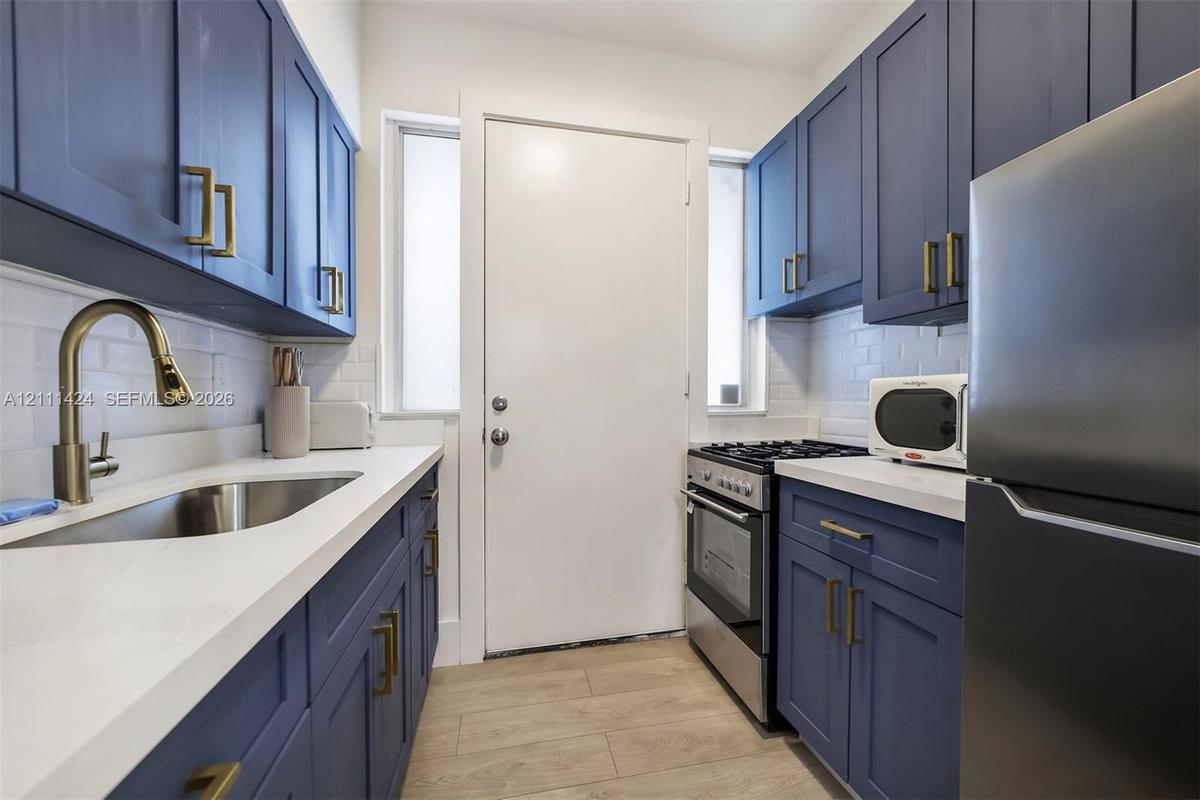 Navy blue cabinetry with brass-finish hardware, white composite countertops, white subway tile backsplash, stainless steel sink with pull-down faucet,