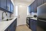 Navy blue cabinetry with brass-finish hardware, white composite countertops, white subway tile backsplash, stainless steel sink with pull-down faucet,