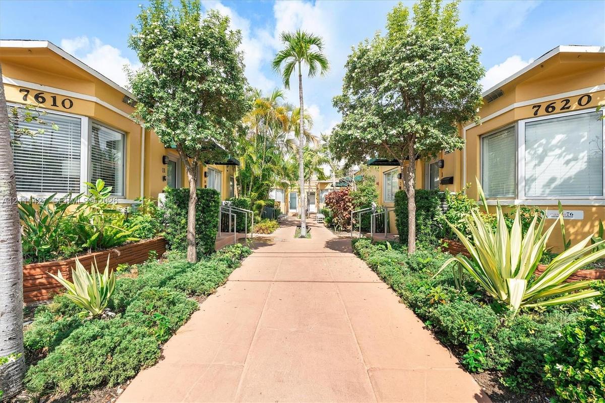 Exterior courtyard featuring a concrete walkway, lush tropical landscaping, mature trees, and building facades with large glass windows