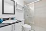 Bathroom featuring a vanity with a dark countertop and oval undermount sink, black-framed mirror, mounted shelving, and a shower enclosure with large-