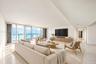 Expansive living space featuring floor-to-ceiling glass panel doors, a balcony with a metal railing, polished stone flooring, and a built-in wood-fini