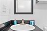 Bathroom vanity featuring a dark solid-surface countertop, an integrated white oval sink, and a high-arch metal faucet, accented by a black-framed wal