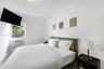 Bright bedroom featuring neutral walls, a single-pane window with exterior greenery, and an installed wall-mounted air conditioning unit