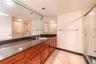 Full-width vanity featuring dark stone-finish countertop, undermount sink, recessed lighting, expansive wall-to-wall mirror, and wood-finish cabinetry