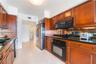 Kitchen featuring warm-toned wood cabinetry, dark stone countertops, mirror backsplash, stainless steel appliances, and tile flooring