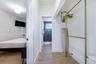 Hallway with wood-finish flooring leading to the bathroom, with a view into a bedroom and a gold-tone clothing rack