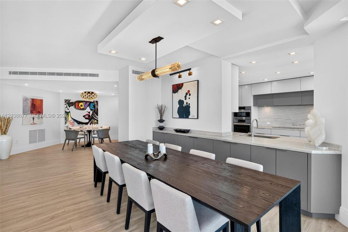 Open-concept dining space space featuring wood look plank porcelain flooring, a coffered ceiling with recessed lighting, minimalist flat-panel cabinet