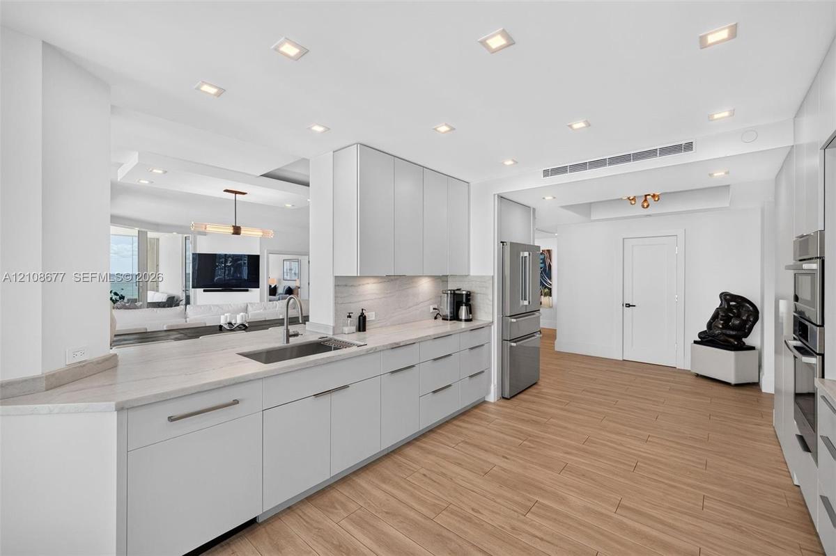 Kitchen featuring flat-panel cabinets, light-toned stone counters, stainless appliances including a wall ovens, recessed lighting, and wood look plank