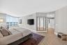 Expansive window wall with water view, wood look plank porcelain flooring, and built-in mirror paneling. Light-filled ovesized primary bedroom featuri