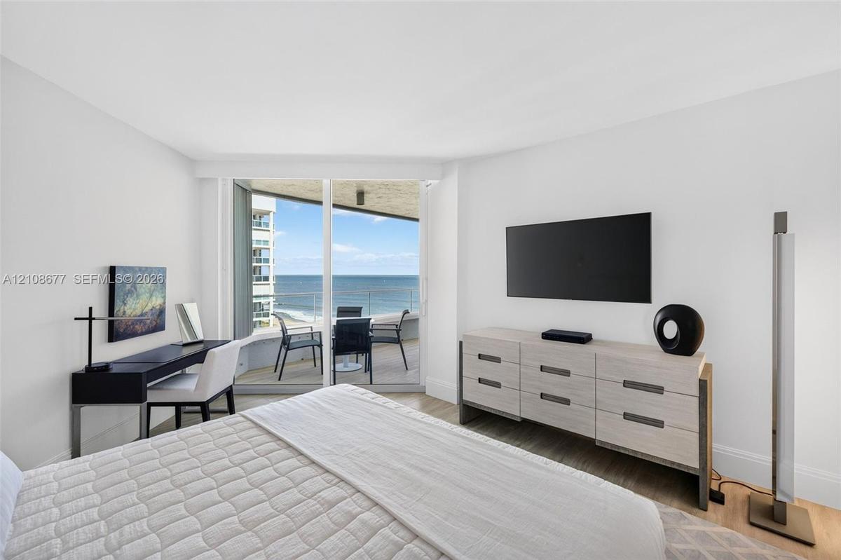 Full-height sliding glass doors opening to a private balcony, wood look plank porcelain flooring, and expansive ocean views. Double layered (light fil