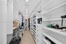 View toward long side of the custom walk-in closet featuring floor-to-ceiling white shelving, integrated cabinetry with drawers, multiple hanging rods