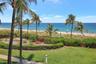 Oceanfront grounds featuring a landscaped lawn, groomed hedges, mature palm trees, and a stone-paver walkway