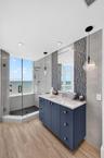 Custom navy-blue vanity with a stone countertop, glass-enclosed shower with tiled flooring, wood look plank porcelain flooring, and accent tile backsp