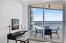 Full-height sliding glass doors opening to a private balcony with glass railing, wood look plank porcelain flooring, and ocean scenery. Double layered