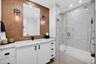 Bathroom featuring a hammered metallic tile accent wall, white floating vanity with stone counters, undermount sink, frameless glass shower enclosure,